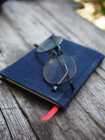 Notebook and eyeglasses on a wooden table in the gardenの写真素材