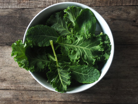 Fresh green kale leaves in bowl on wooden table, top view. Organic foodの写真素材