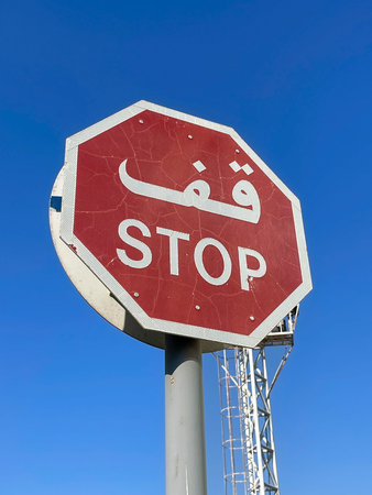 Red octagonal stop sign with Arabic and English text under blue sky, Dubai 18.01.2025 United Arab Emirates.のeditorial素材