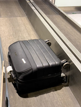 Baggage claim at the airport, a black suitcase on the conveyor belt in the arrivals area. Concepts of travel, transportation, and baggage claim.の写真素材