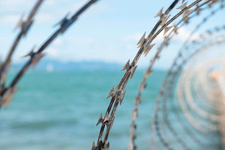 Razor Wire Fence with Shallow Depth of Field Against a Blurred Ocean Background, High Contrast Industrial Security and Border Protection Photography. Nha Trang 20.12.2025 Vietnamの写真素材