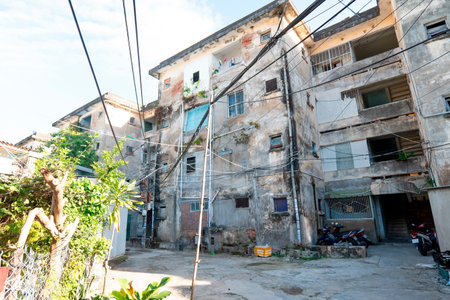 A multi-story weathered concrete apartment block with exposed brick and tangled overhead utility wires above a paved courtyard with parked scooter bikes. Nha Trang 20.12.2025 Vietnamのeditorial素材