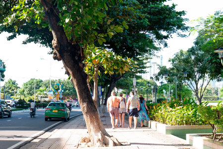 Group of International Tourists Walking on Sunny Tropical City Sidewalk with Lush Green Trees and Urban Traffic Background, High Key Natural Lighting Nha Trang 20.12.2025 Vietnamのeditorial素材