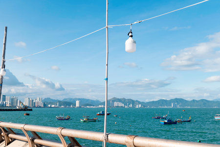 Traditional Fishing Boats Floating on Turquoise Sea with Modern City Skyline and Mountains, Bright Sunny Day in Nha Trang Vietnam, Coastal Scenery Nha Trang 20.12.2025 Vietnamの写真素材