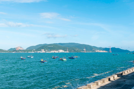 Small wooden fishing boats float in a turquoise bay. The background includes green mountains, a ferris wheel, and a blue sky over coastal ocean waters. Nha Trang 20.12.2025 Vietnamのeditorial素材
