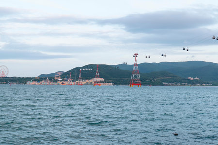 Cable car system with red lattice towers crossing over sea water towards a coastal resort and...