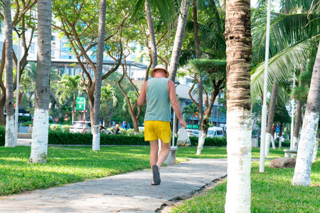 Senior Male Tourist Walking Through Tropical Palm Tree Park in Bright Sunlight, Lifestyle Travel and Retirement Freedom in Coastal City Resort Environment Nha Trang 20.12.2025 Vietnamのeditorial素材