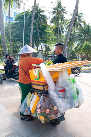 Authentic Vietnamese Street Food Vendor on Motorbike with Conical Hat and Fresh Fruit, Tropical Daylight, Wide-Angle View of Local Asian Lifestyle and Urban Tourism. Nha Trang 20.12.2025 Vietnamのeditorial素材
