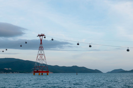 Cable car cabins suspended on steel cables above sea water with a red and white lattice support...