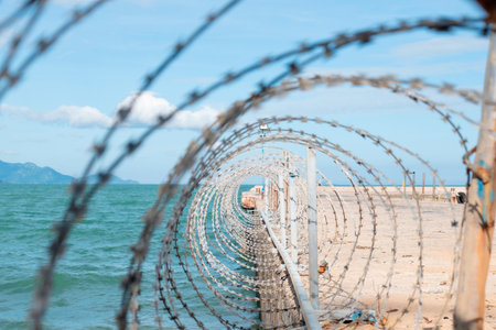 Coiled Razor Wire Security Fence on Coastal Pier with Turquoise Sea Background, Sharp Selective Focus and Depth of Field for Border Protection Concept Nha Trang 20.12.2025 Vietnamの写真素材