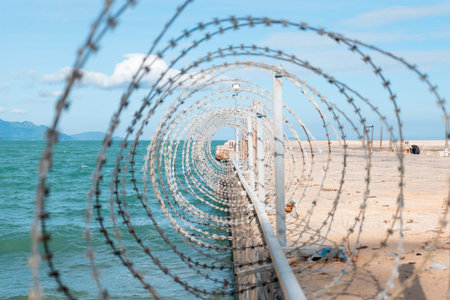 Coiled Razor Wire Fence on Coastal Border Pier with Cinematic Depth of Field and Bright Blue Ocean...