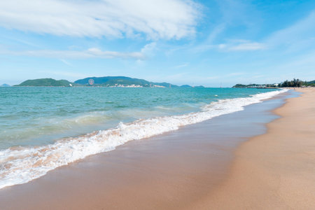 Wide angle cinematic shot of a tropical beach coastline with turquoise water and soft white waves crashing on golden sand under a bright blue sky. Nha Trang 20.12.2025 Vietnamのeditorial素材