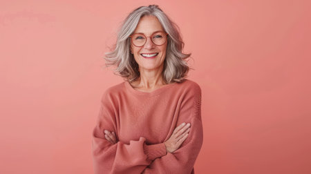 Portrait of a senior woman with gray hair and glasses on a pink background.の素材
