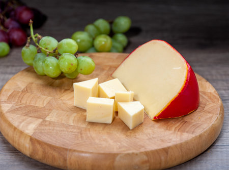 Edam cheese on wooden cutting board with grapesの写真素材