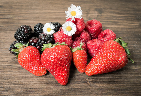 Strawberries and berries adorned with field daisies, on a table. It is a good and fresh fruit that contains few sugars.の写真素材