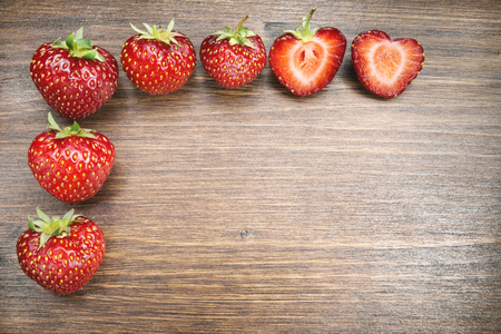 Strawberries on an old country table. With a strawberry cut in half that almost seems to form a heart. A typical summer fruit that is the season of love.の写真素材