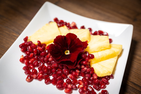 A fruits composition consisting of: pineapple, pomegranate and an edible flower as decorationの写真素材