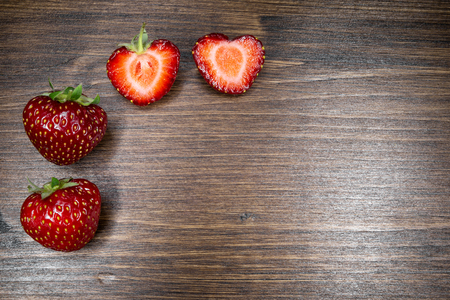 Strawberries on an old country table. With a strawberry cut in half that almost seems to form a heart. A typical summer fruit that is the season of love.の写真素材
