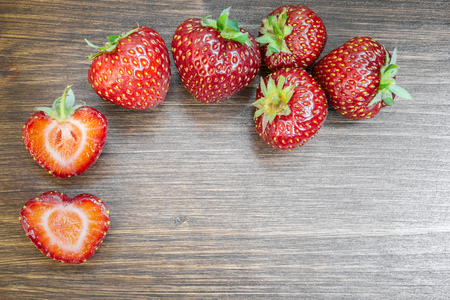 Strawberries on an old country table. With a strawberry cut in half that almost seems to form a heart. A typical summer fruit that is the season of love.の写真素材