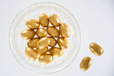 High angle view of a variety of golden wrapped  Easter chocolate eggs on a plate and white...