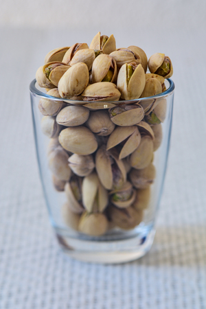 Closeup of a glass full of pistachio nuts on a white backgroundの写真素材