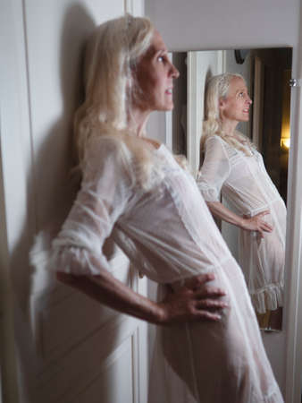 Vertical profile portrait of a glamourous woman in lingerie standing by a doorの写真素材