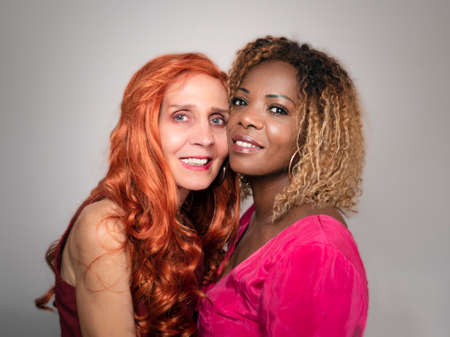 Horizontal portrait of two elegant and beautiful black and white women friends wearing summer hatsの写真素材
