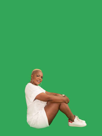 Vertical portrait of a smiling beautiful Afro American woman wearing sportswear seating isolated against a green backgroundの写真素材