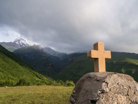 Stone cross next to Gergeti Tsminda Sameba church with mount Kazbeg in the background  