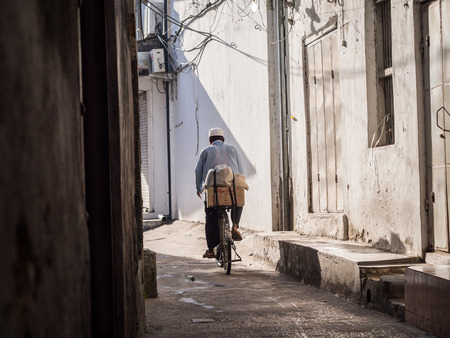 Man biking on one of the streets of Stone Town, the capital of Zanzibar. Stone town is known for its colonial architecture.のeditorial素材