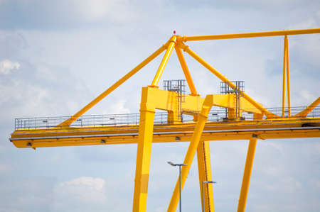 Yellow gantry crane opposite cloudy sky. Industrial lifting machinery.