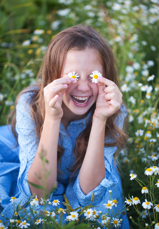 Beautiful young woman lying on grass and smelling flower, against background of summer green park.の写真素材