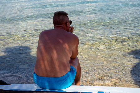 A man in a blue swimsuit sits on a boat and looks at the seaの写真素材