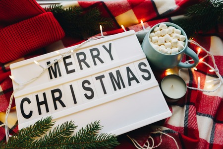 Merry Christmas text displayed on a light box. Christmas decoration and coffee cup with marshmellow on the red plaid. Christmas holiday mood concept. Flat lay. Top viewの写真素材