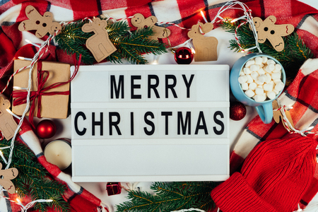 Merry Christmas text displayed on a lightbox with beautiful Christmas decoration with fir branches, red plaid and lights. Flat lay. Top viewの写真素材