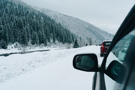 Side view of the black car on the winter road near the beautiful pine tree forest covered with snow.