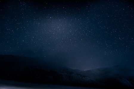 Beautiful blue dark night sky with many stars above snowy mountainsの写真素材