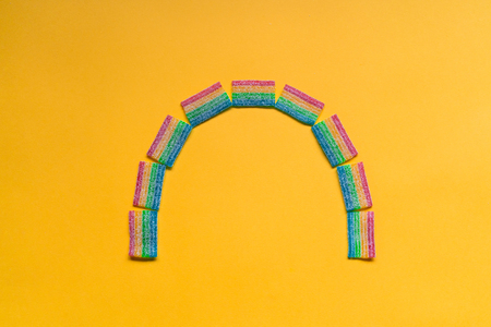 Colorful chewy sour candies arranged as rainbow, isolated on yellow background. Rainbow shapeの写真素材