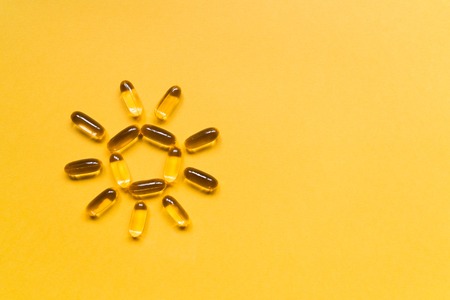 Close up capsules of fish fat oil in the sun shape, omega 3, vitamin e on the yellow background. Healthy food diet. Nutritional supplementの写真素材