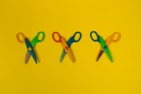 Safety colorful scissors isolated on the yellow background. Three colorful kids scissors. Zigzag, wave shapeの写真素材