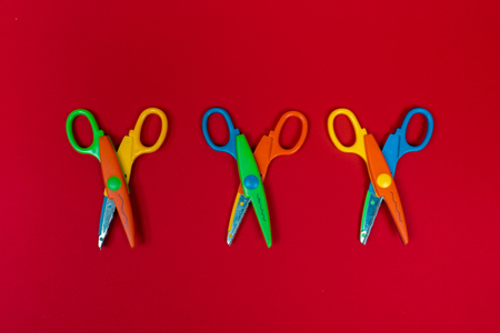 Safety colorful scissors isolated on red background. Three colorful kids scissors. Zigzag, wave shapeの写真素材