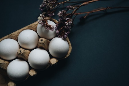 Beautiful Easter eggs concept. White easter eggs in carton box and dried flowers isolated on black dark background.の写真素材