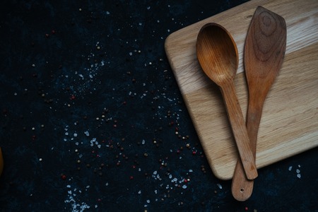 Wooden spatula and a spoon for frying on pans on a wooden cutting board isolated on black table...
