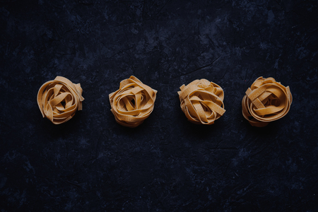 Traditional italian raw pasta fettuccine isolated on the black stone background. Top view. Four egg nests noodles.の写真素材