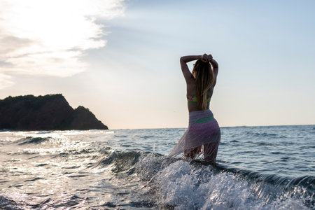 A girl in a bikini swims in the sea against the background of the sunset.