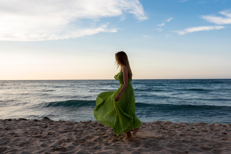 Young beautiful woman in green dress walking on the beach at sunset.の写真素材