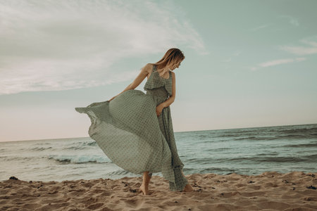 Beautiful young woman in long dress on the beach at sunset.の写真素材