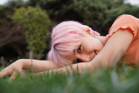 Young lesbian LGBT woman with pink hair poses smilingly in the park