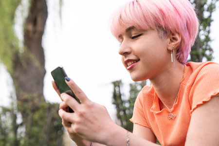 Young girl with pink hair writes a message on her mobile phone