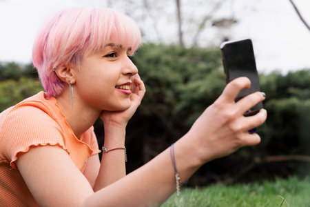 A girl with pink hair is taking a selfie with her cell phoneの写真素材